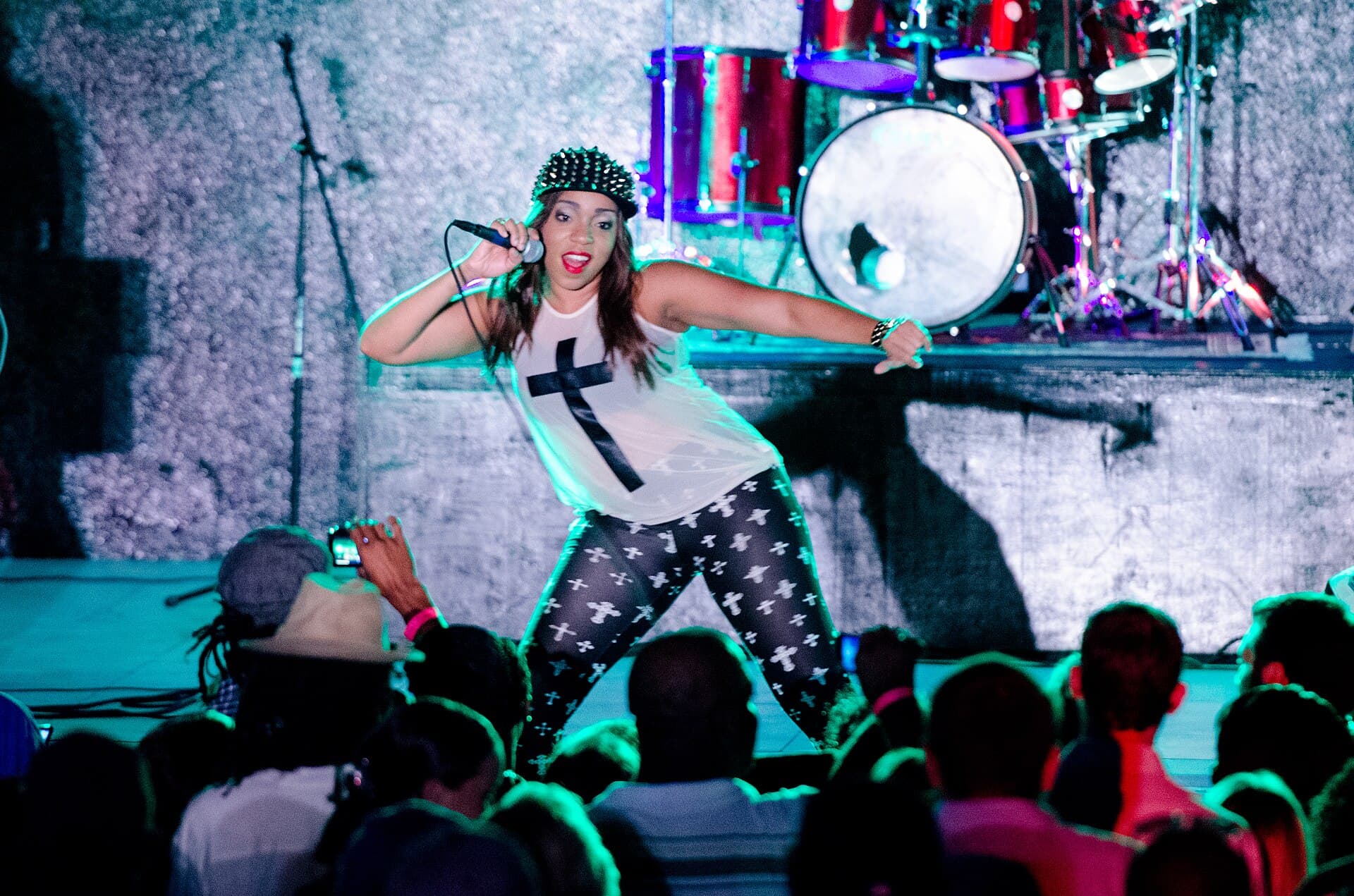Destra Garcia in a cap, white top and patterned leggings striking a pose with a microphone on stage in front of a crowd in 2013