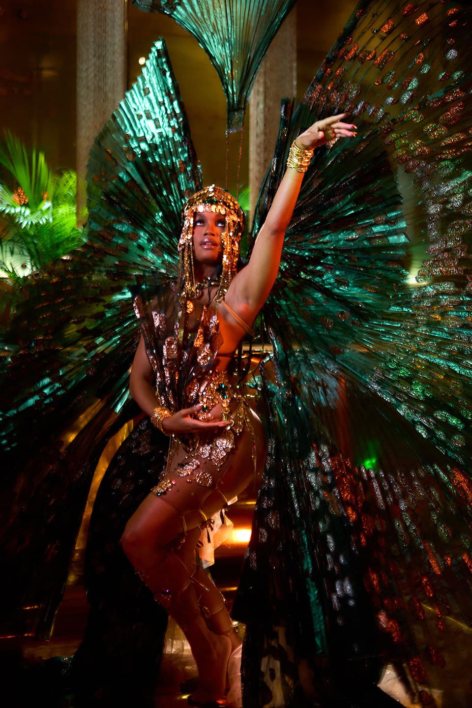 The Lost Tribe 2027 Stories of the Sand promo: masquerader in a gold sequinned costume and headdress with a large teal fan backpiece